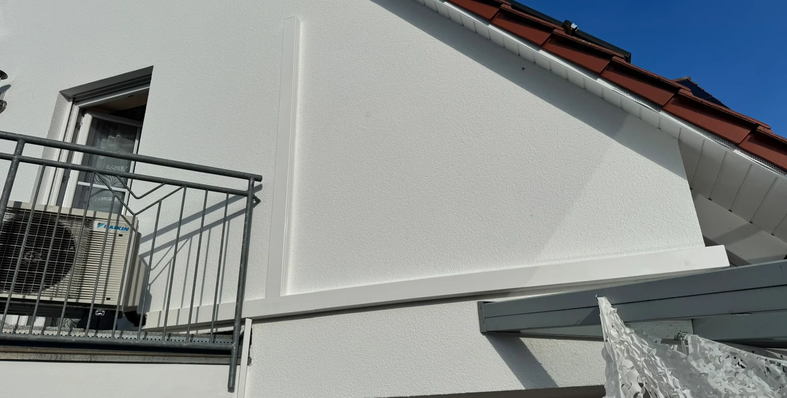 Weißer Leitungskanal entlang einer hellen Hausfassade